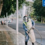 a man in a yellow vest is spraying water on a sidewalk